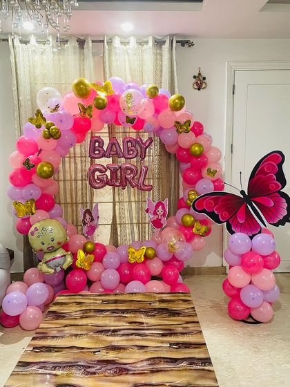 For this "Baby Girl" welcome party, I combined a circular balloon arch with a butterfly theme. The decoration uses pink, purple, and gold balloons, along with a large butterfly prop and baby-themed foil balloons.