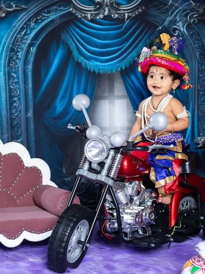 Our little Krishna is enjoying his ride on a toy motorcycle, blending tradition with modern fun.
