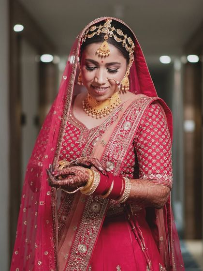 A close-up of the bride in her red wedding attire, her gaze lowered in a moment of quiet contemplation.