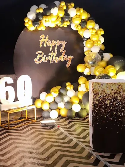 An elegant and sophisticated setup for a 60th birthday celebration. The classic black and gold balloon arch frames a personalized backdrop, complemented by large marquee numbers and a stylishly decorated cake plinth.