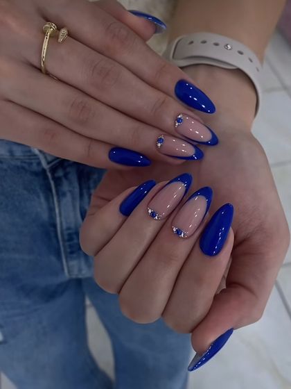 A striking royal blue manicure on almond nails, with a negative space French design accented by carefully placed blue rhinestones.