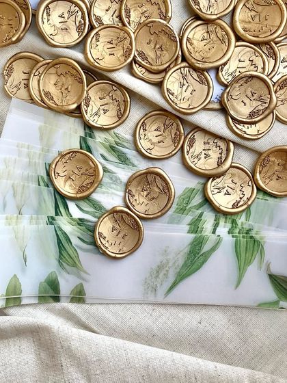 A collection of custom gold wax seals, each stamped with the couple's initials. These were used to seal delicate vellum wraps around the invitations, adding a classic and personal touch.