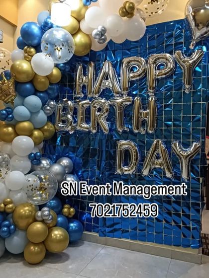 A bold blue and gold home decoration. The balloon garland is set against a blue metallic foil curtain with large "Happy Birthday" letters, creating a vibrant look.
