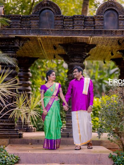 A couple in traditional South Indian attire walks through our stone pillar hall, a perfect setting for a classic and elegant photoshoot.