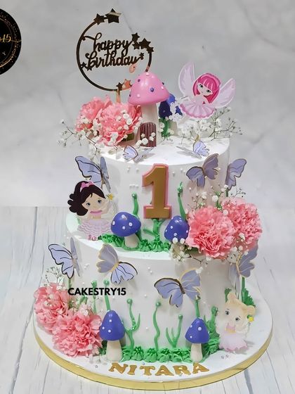 A beautiful fairy-themed cake for a first birthday. This choco-chip cake is decorated with fresh carnations, baby's breath, and delicate fairy and butterfly toppers for an enchanted garden look.