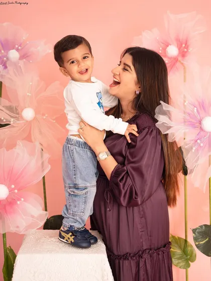 A mother and son share a laugh during their Mother's Day photoshoot. The whimsical pink flower backdrop adds a touch of magic to this happy portrait.