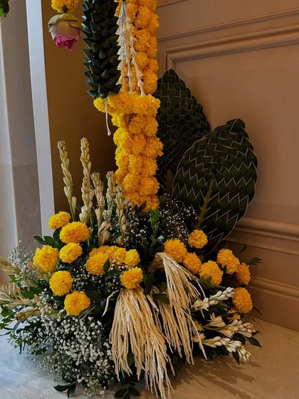 A beautiful floor arrangement for a housewarming, combining vibrant marigolds with woven palm leaves and other traditional greens for a festive and auspicious look.
