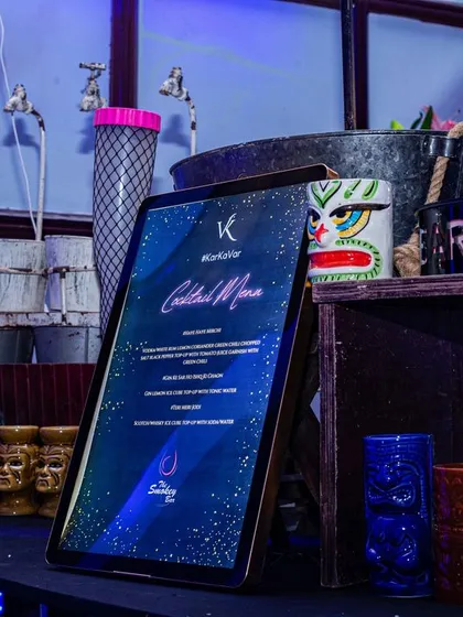 A detailed look at a themed bar corner. I use custom cocktail menus on digital screens and unique props like tiki mugs and leg-shaped glasses to match any party theme you can imagine.