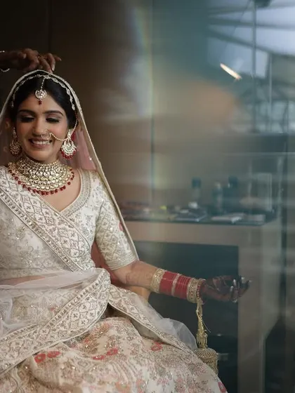 A candid shot of Kanika getting her final touches. The soft lighting highlights the clean, elegant lines of her makeup and the beautiful details of her bridal attire.