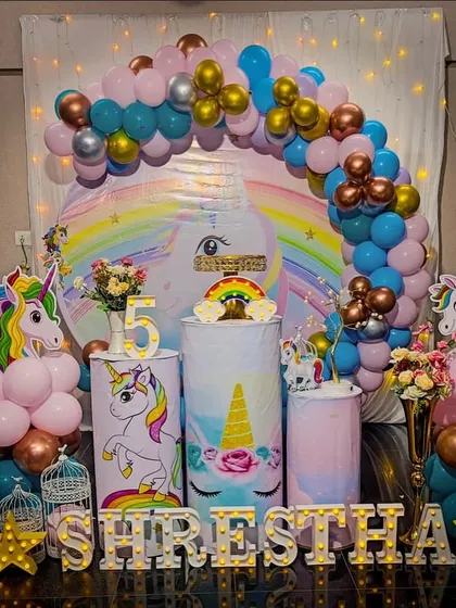 A vibrant unicorn theme for a 5th birthday, featuring a circular backdrop, a light-up number '5', and unicorn-themed plinths for the cake display.