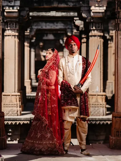 A formal portrait of the couple in their royal attire. The intricate architecture of the Gujarat stepwell provides a stunning, symmetrical backdrop that enhances their regal presence.