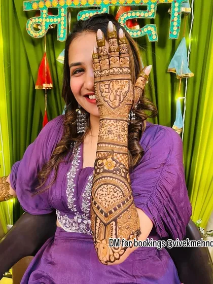 A happy bride posing with her personalized mehndi, featuring her initial 'N' prominently on the palm.