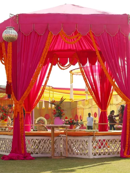 A vibrant Mehendi or Haldi setup with a fuchsia pink tent draped with marigold garlands. This design uses bold colors to create a festive and energetic atmosphere.