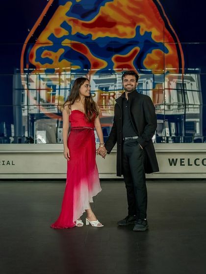 The couple stands inside the modern lobby of the Imperial College, holding hands. The colorful art installation in the background adds a unique and vibrant touch to this urban portrait.