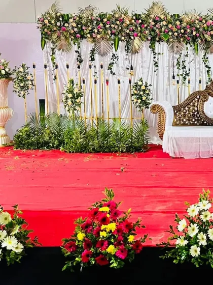 Here is a closer look at a simple yet beautiful reception stage. The focus is on the floral garland across the top, the elegant carved sofa, and the simple white curtain backdrop, showing that a clean design can be very effective.
