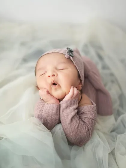 Another adorable sleepy expression, with chubby cheeks squished between tiny hands. This classic newborn pose is a favorite among parents.