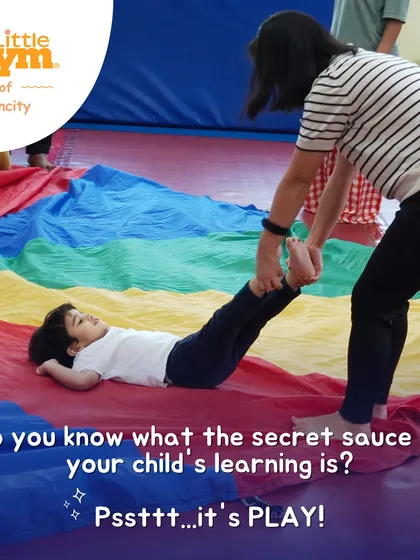 The secret to learning is play. A child enjoys a ride on the colorful parachute, a group activity that builds core strength and teaches cooperation.