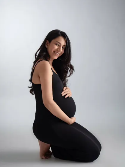 A simple and elegant kneeling portrait in a classic black dress. The clean grey background puts all the focus on the mother-to-be's happy expression and beautiful bump.