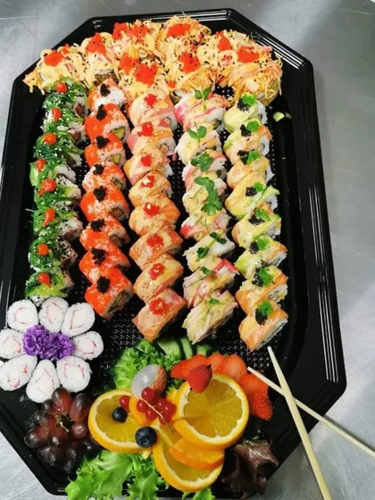 For sushi lovers, we offer large, assorted platters that are perfect for sharing. This platter includes a wide variety of rolls, from classic California rolls to spicy tuna and vegetarian options, garnished with fresh fruit.