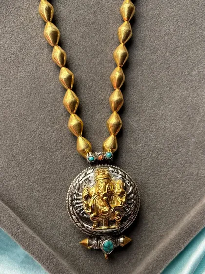 A bold dual-tone pendant necklace featuring a gold-plated Ganesha motif set against an oxidised silver background. The piece is strung on a substantial gold-beaded chain, making it a powerful statement of faith and style.