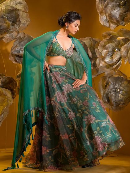 This printed and embroidered skirt set by Q by Sonia Baderia blends fierce femininity with detailed craftsmanship. The vibrant green, modern cut-out blouse, and flowing cape make it an ideal choice for cocktail nights or destination weddings.