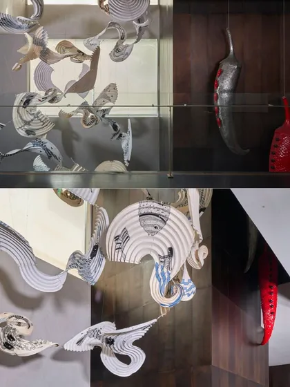 A detailed look at a cascading origami light installation. The interplay of folded parchment and light creates a dynamic visual effect, while a bold red chili sculpture by Subodh Kerkar adds a surprising, artistic counterpoint.