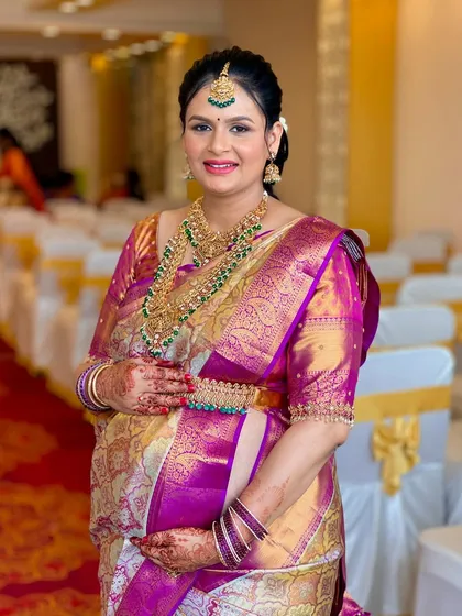 Usha looking absolutely radiant for her Seemantham. Her look features a stunning magenta and gold Kanjeevaram saree, paired with intricate temple jewelry and a makeup look that highlights her happiness.