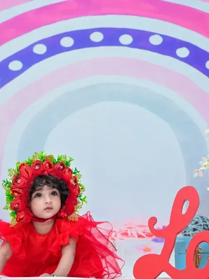 A wider view of the rainbow-themed setup, with the word "Love" and floral decorations. The baby sits sweetly in her red outfit, creating a beautiful and colorful scene.