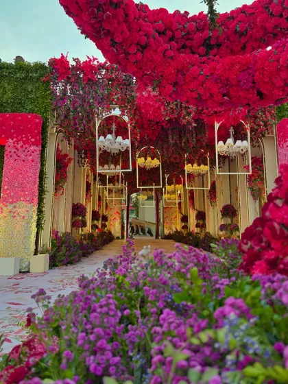A view of the entrance walkway, lined with a garden of purple flowers and leading towards a tunnel of red blooms. The design creates a journey of color.