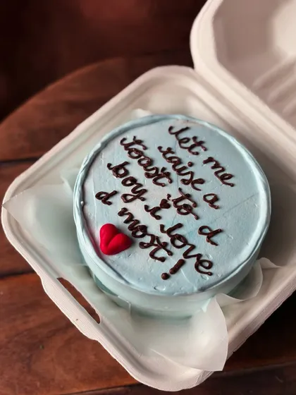 This bento cake features a sweet message: "let me raise a toast to a boy i love d most!". It's a personal and heartfelt way to show someone you care.