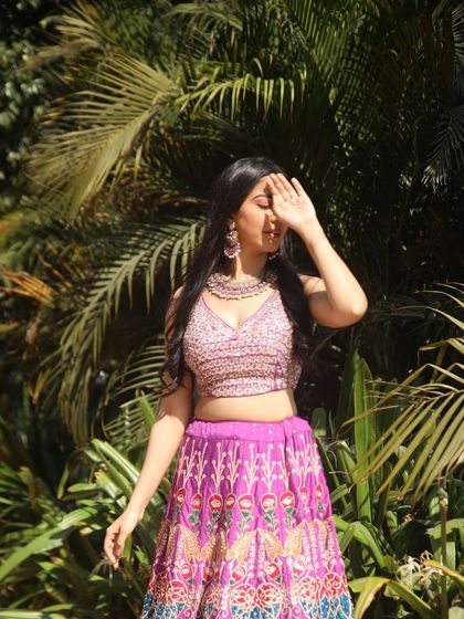 A playful, sun-shielding pose that adds a touch of drama and highlights the sequined blouse against a lush green background.