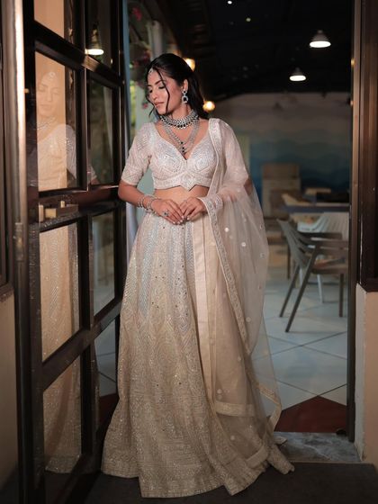 A candid shot of a model in a white lehenga, showing the full outfit in a relaxed setting. The simple diamond jewellery adds a touch of sparkle.