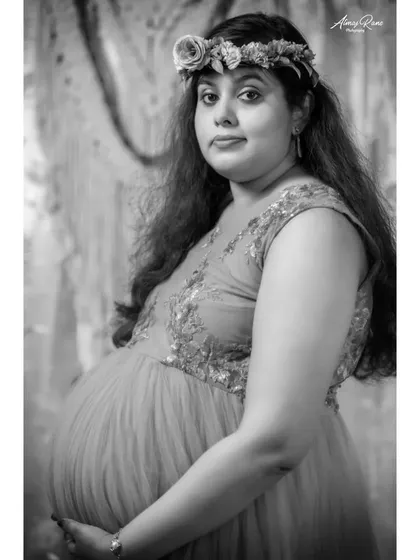 The same studio portrait, presented in classic black and white. This version emphasizes the mother's expression and the soft textures of the gown and floral crown.