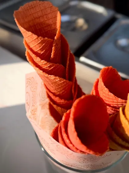 A stack of brightly colored, freshly made waffle cones, ready to be filled with our artisanal gelato. This simple, colorful shot emphasizes the fresh, from-scratch elements of our dessert stations.
