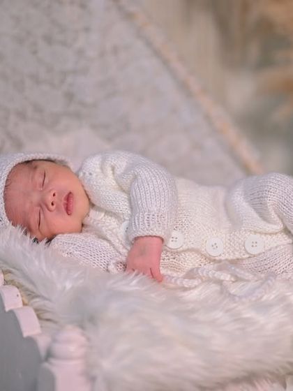 A full-length view of the newborn in an all-white knitted outfit, sleeping soundly on a tiny bed.