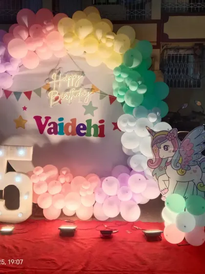 A magical unicorn theme for a 5th birthday party. The setup includes a circular backdrop, pastel rainbow balloon decor, unicorn cutouts, and a large light-up number '5'.