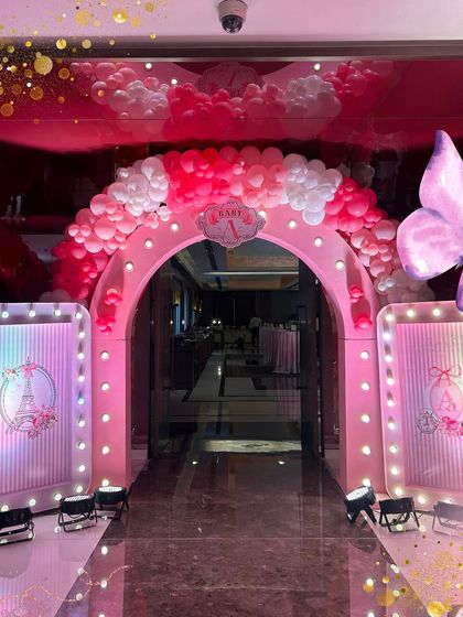 A grand entrance arch in shades of pink, white, and red, illuminated by marquee-style lights. This sets a glamorous tone for a Paris-themed pink baby shower.