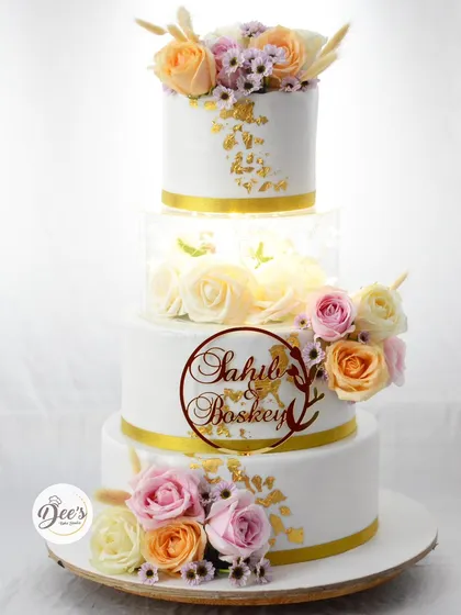 A wedding cake should be as timeless as your love story. This four-tier beauty features an illuminated acrylic section filled with roses, delicate sugar flowers, and touches of edible gold leaf for a truly showstopping centerpiece.