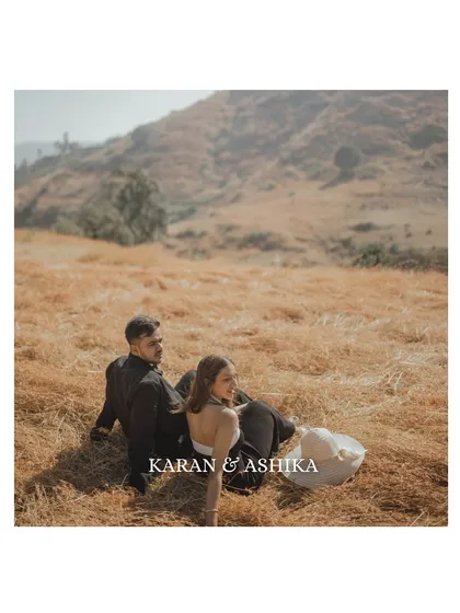 The couple sits together in a field of golden grass, looking out at the landscape. This quiet, contemplative shot captures a moment of shared peace and connection.