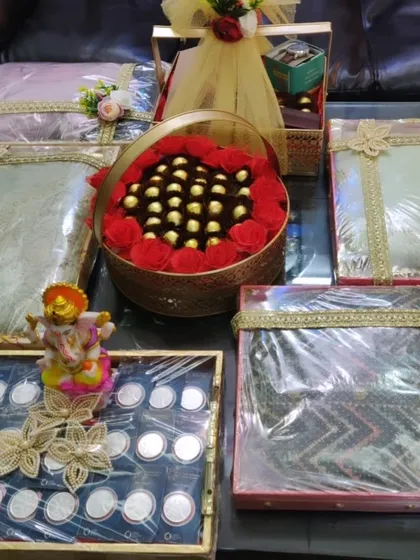 This image showcases a full trousseau and sagan collection ready for a wedding. You can see multiple packed outfits, a tray of silver coins, and a central chocolate basket, all coordinated to create a grand and festive display.