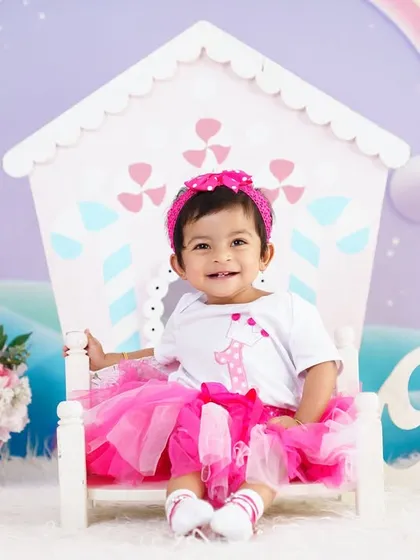 A bright and happy first birthday shoot with a pink tutu and a colorful dollhouse backdrop. Her smile lights up the whole scene.