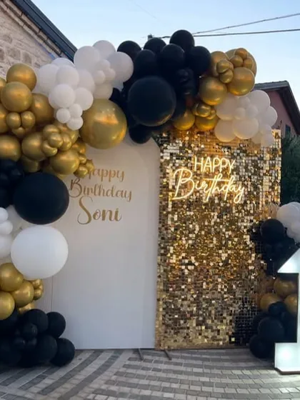 A chic and modern first birthday setup featuring a black, white, and gold color scheme. The gold shimmer wall, custom neon sign, and light-up number '1' create a glamorous photo backdrop for a stylish celebration.