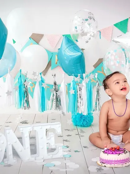 A first birthday is a huge milestone, and a cake smash session is the perfect way to celebrate. This little one is having a blast with his cake, surrounded by a custom blue and white balloon setup complete with a light-up "ONE" sign.
