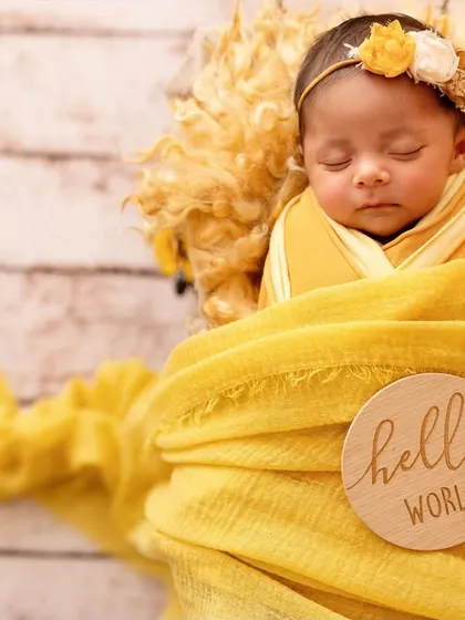 "Hello World!" This little one is perfectly swaddled in a yellow wrap, announcing her arrival in style. The wooden sign adds a lovely personal touch.