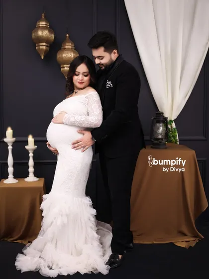 The dad-to-be joins for a loving embrace in this elegant studio setup. Their coordinated black and white outfits create a timeless and classic couple's portrait.