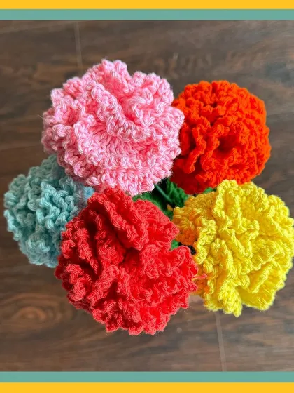 A top-down view of a colorful bunch of crochet carnations. I make these in a variety of colors like pink, red, yellow, orange, and light blue, each with fluffy, textured petals that look just like the real thing.