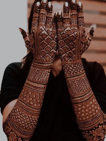A dramatic, dark-stained full bridal mehndi covering the hands and arms completely in a dense web of beautiful, intricate patterns.