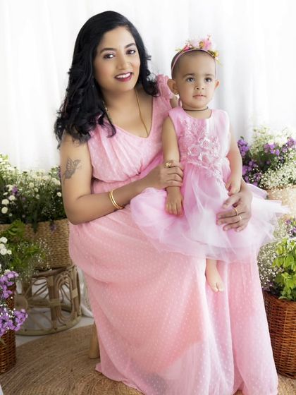 A mother holds her daughter on her lap in this classic Mother's Day portrait, both looking radiant in pink.