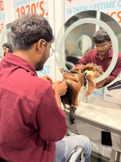 A student carefully applies hair extensions to a mannequin, focusing on clean sectioning and placement.