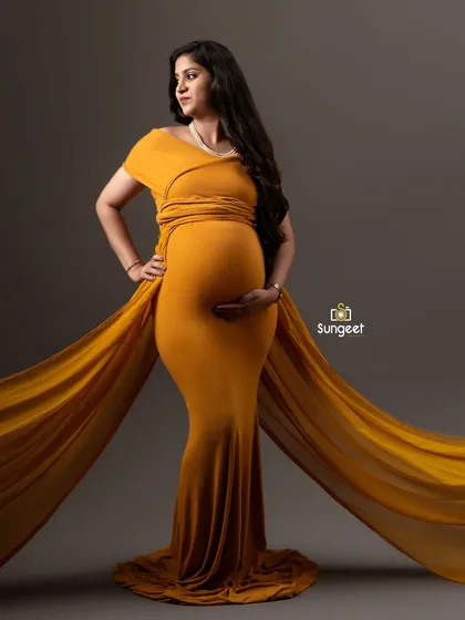 A powerful and classic maternity pose in a mustard yellow infinity gown. The flowing fabric extensions create a dramatic effect.